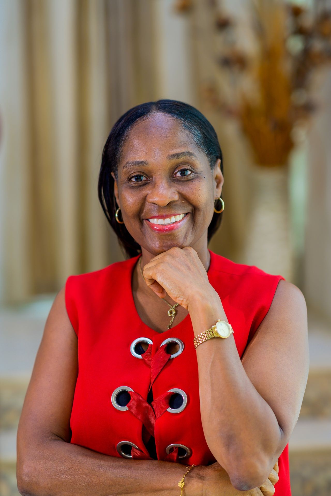 Woman in a red dress smiling with her hand resting on her chin.